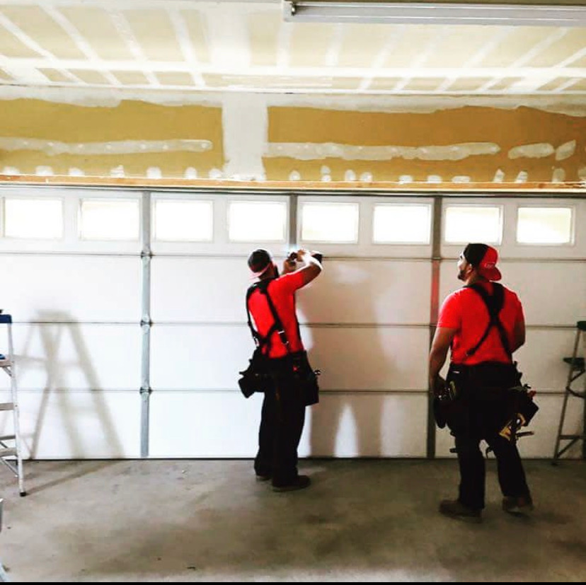 Two Almighty technicians working on a white garage door with window panels